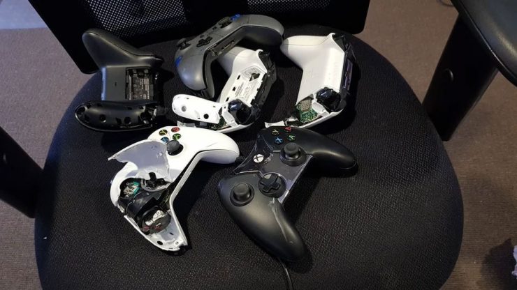 An image showing several controllers, mainly Xbox One control pads, broken, smashed, and ripped to pieces